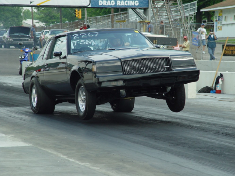 Car performing wheelie at drag racing event.